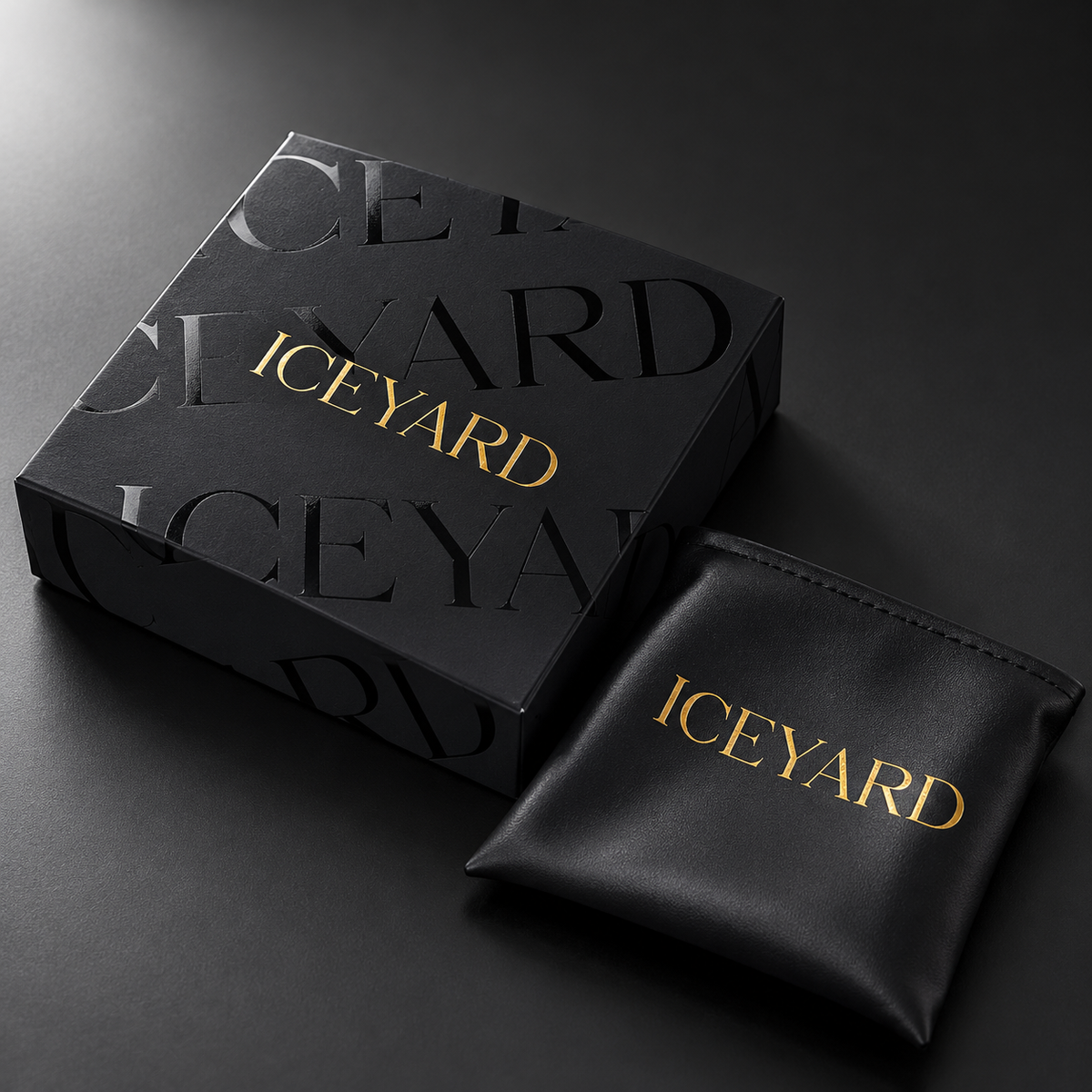 Svart Iceyard-eske med blankt svart mønster, gullogo og en svart PU-smykkepose.