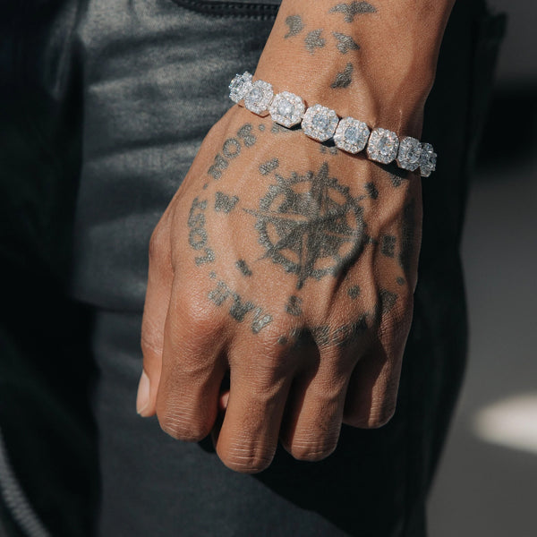 Sølvfarget tennisarmbånd med store, runde steinkluster på et tatovert håndledd.