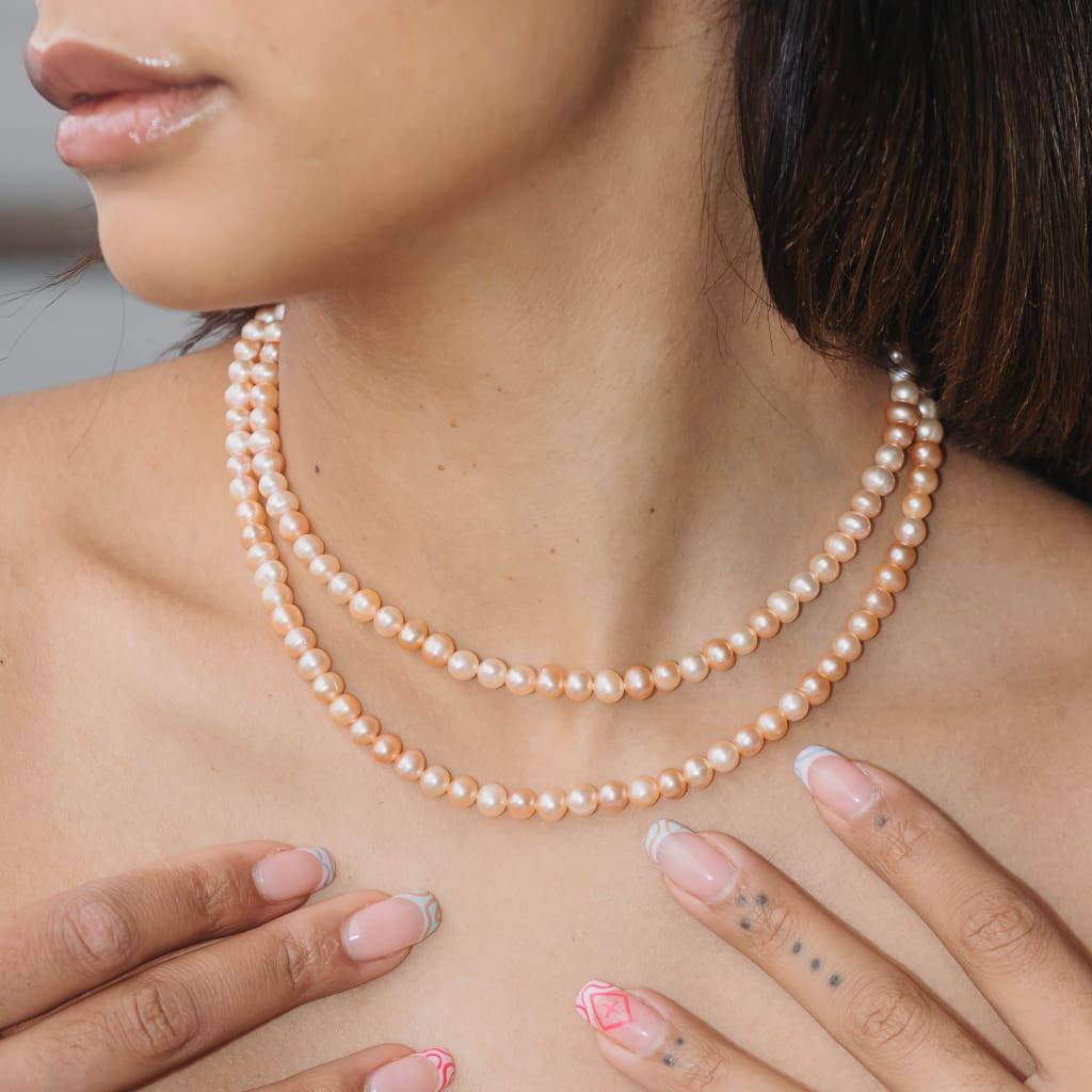 A woman wearing a double-strand pink pearl necklace with a gold-plated metal base.