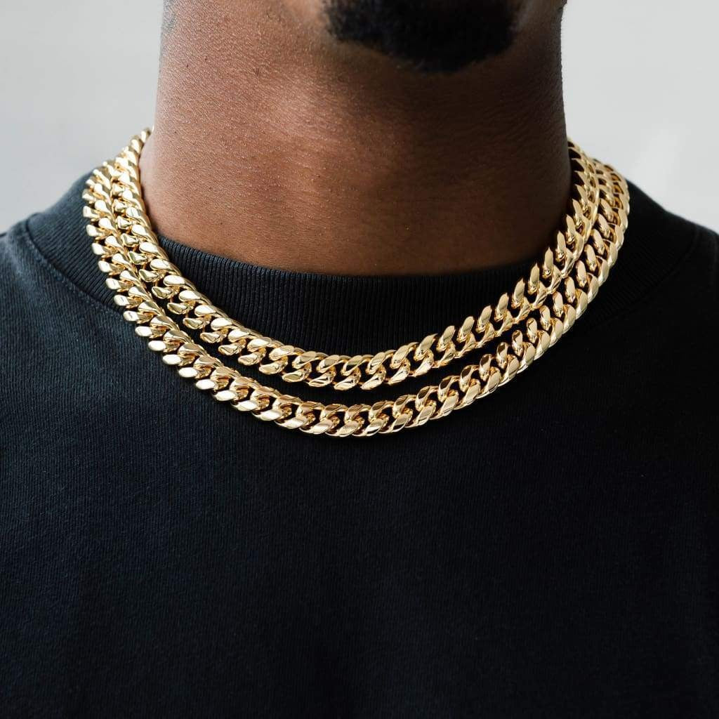 A person wearing a black crew neck t-shirt with a gold-colored Miami Cuban chain necklace.