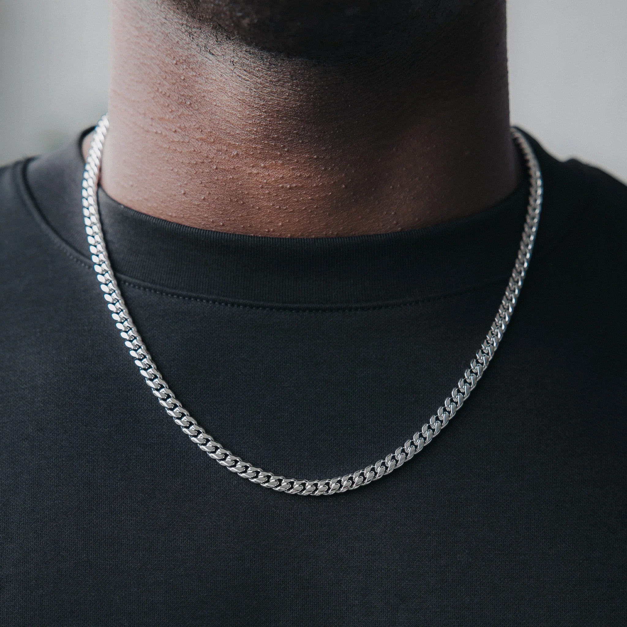 A person wearing a black crew neck sweater showcasing a white gold Miami Cuban link chain necklace.