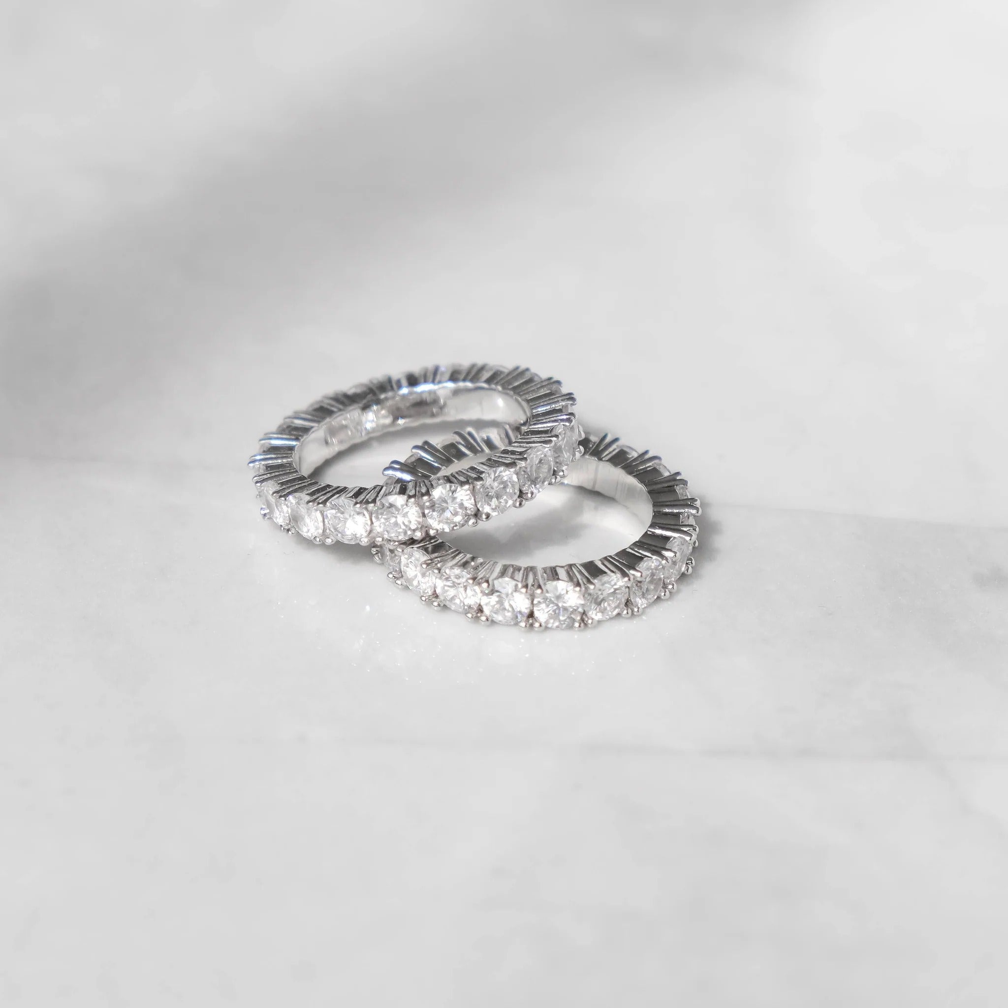 A 14K white gold ring with a row of shimmering stones set on its surface, placed on a marble surface.