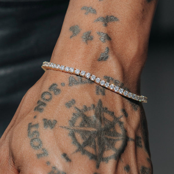 Tynt tennisarmbånd med lyse steiner rundt et tatovert håndledd.