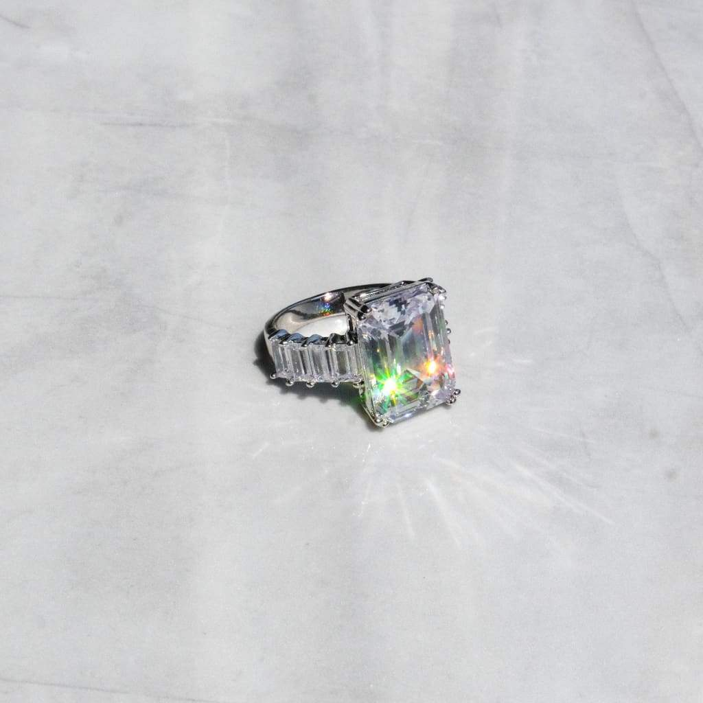 A 14K white gold ring with a clear, emerald-cut CZ stone, set in a classic six-prong setting, displayed on a marble surface.