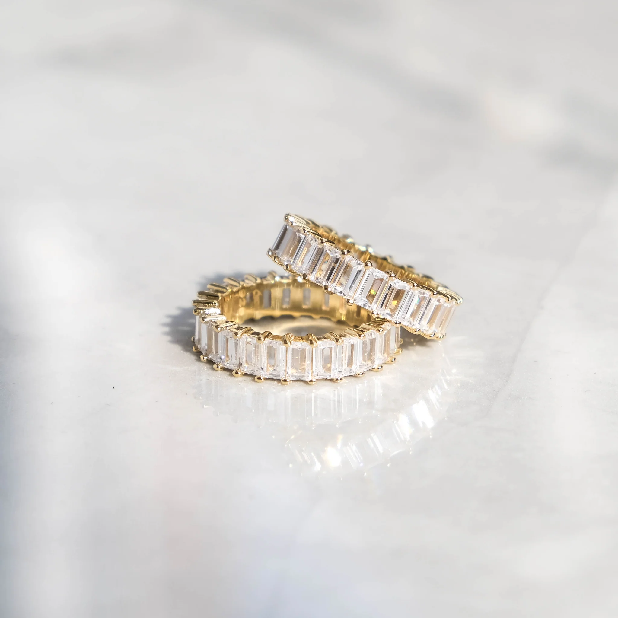 A photo of two rings, one on top of the other, with 18K gold band and AAAA cubic zirconia stones set around the circumference.