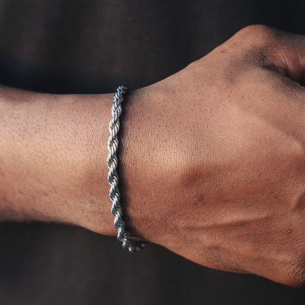 Sølvfarget rope-armbånd med tvunnet lenke rundt et håndledd.