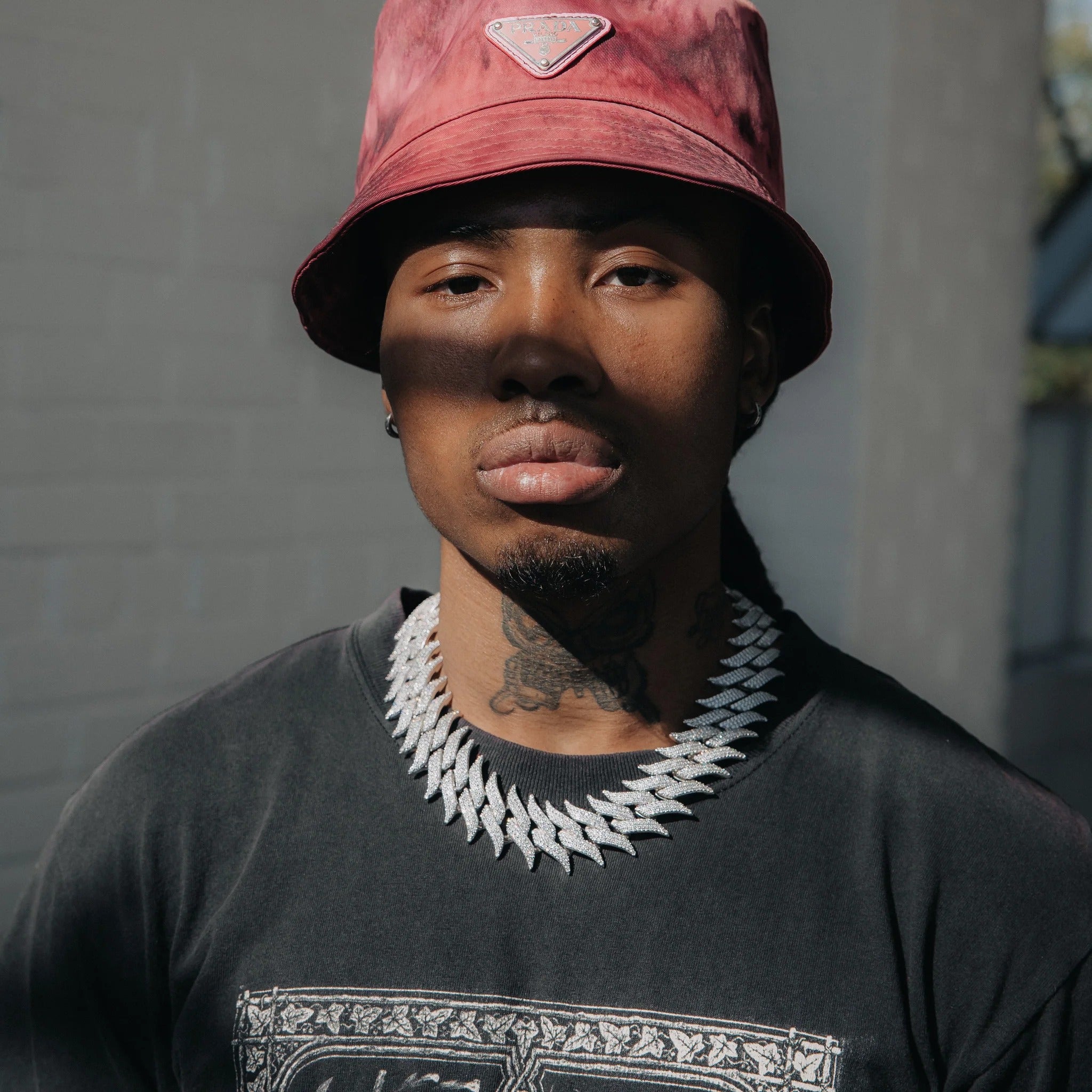 A person wearing a red bucket hat and a spiky white gold necklace with ice-blue stones.