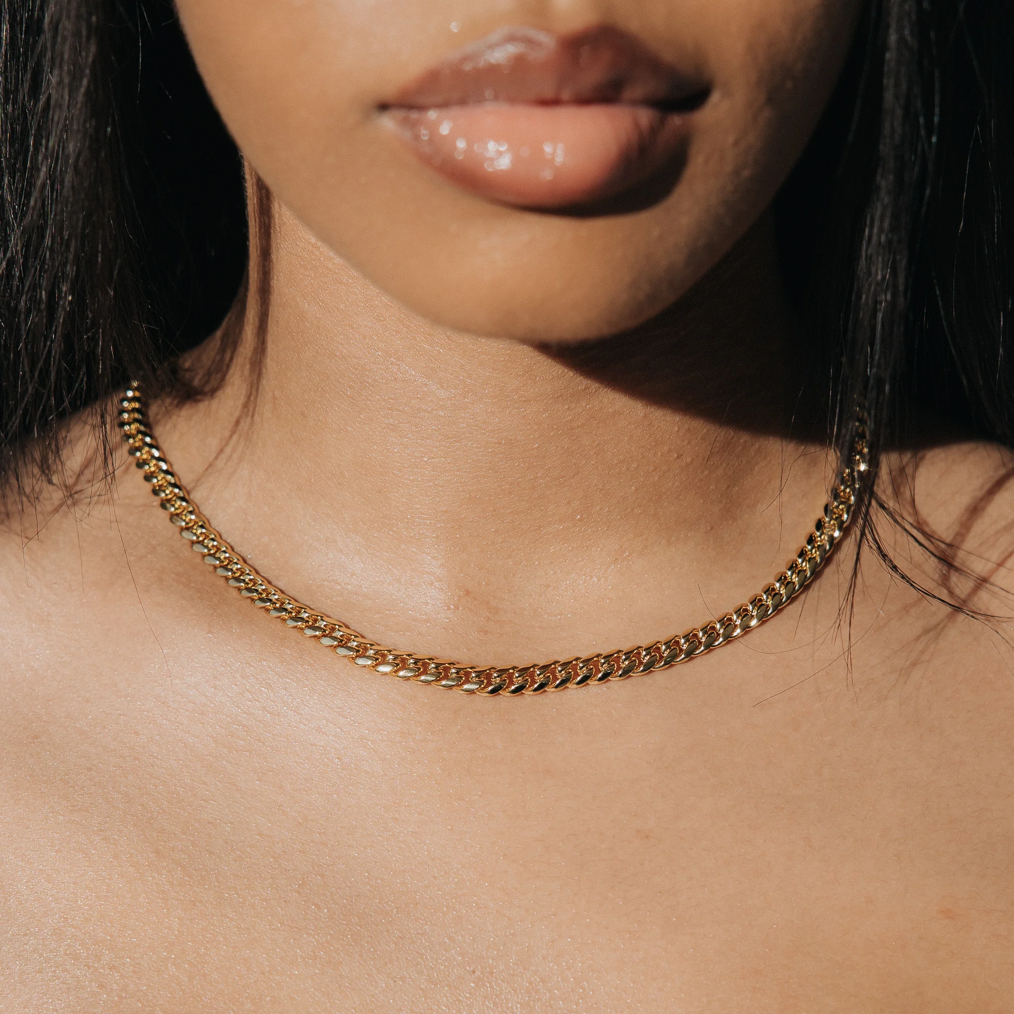 Close-up image of a woman wearing a gold Miami Cuban necklace.