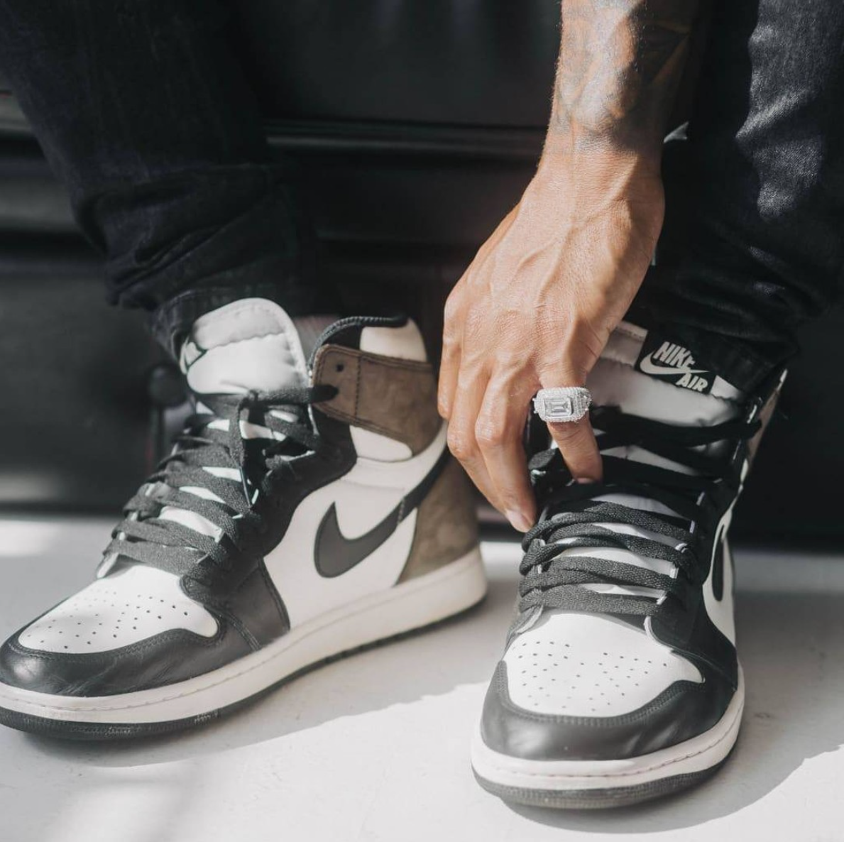 Hånd med en stor steinbesatt ring ved skolissene på et par sneakers