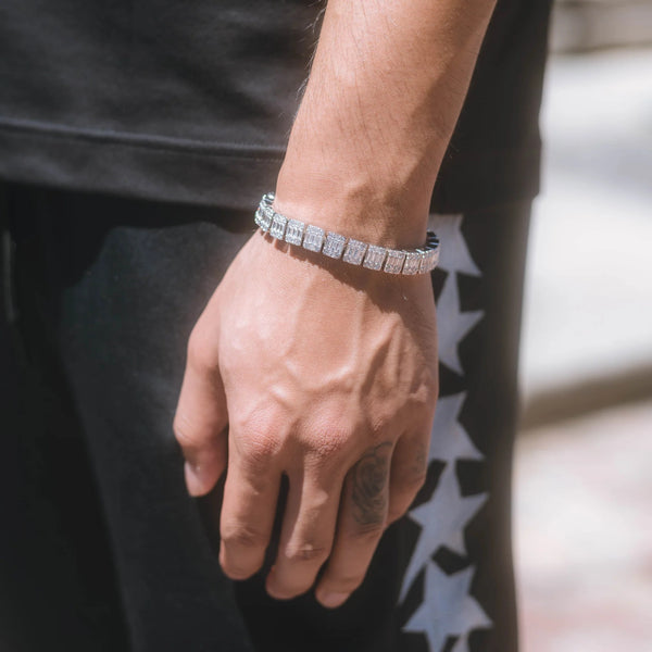 Sølvfarget tennisarmbånd med rektangulære steinfatninger rundt et håndledd.